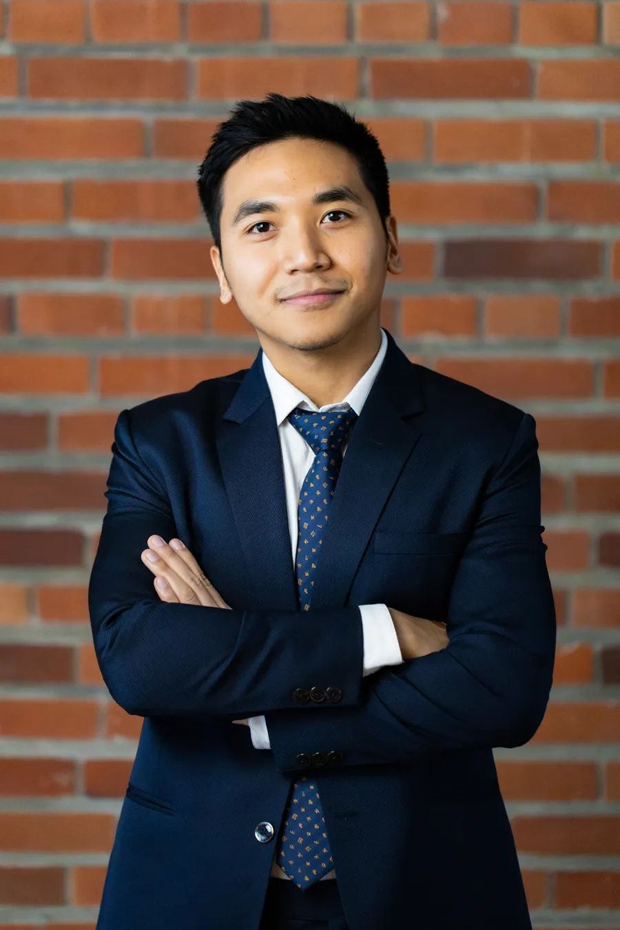 Nikhil Pradhan, in a navy suit, standing against a brick wall